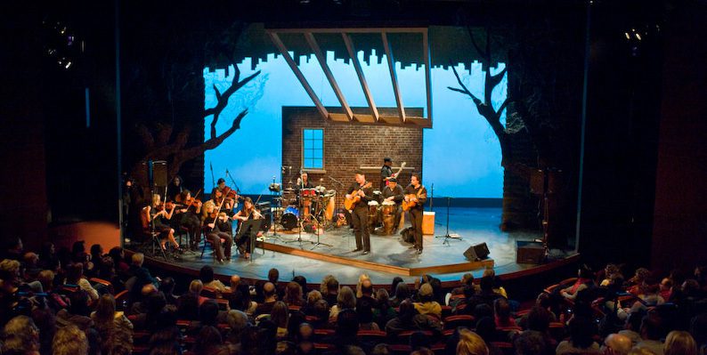 Orchestra performing on stage with audience watching.