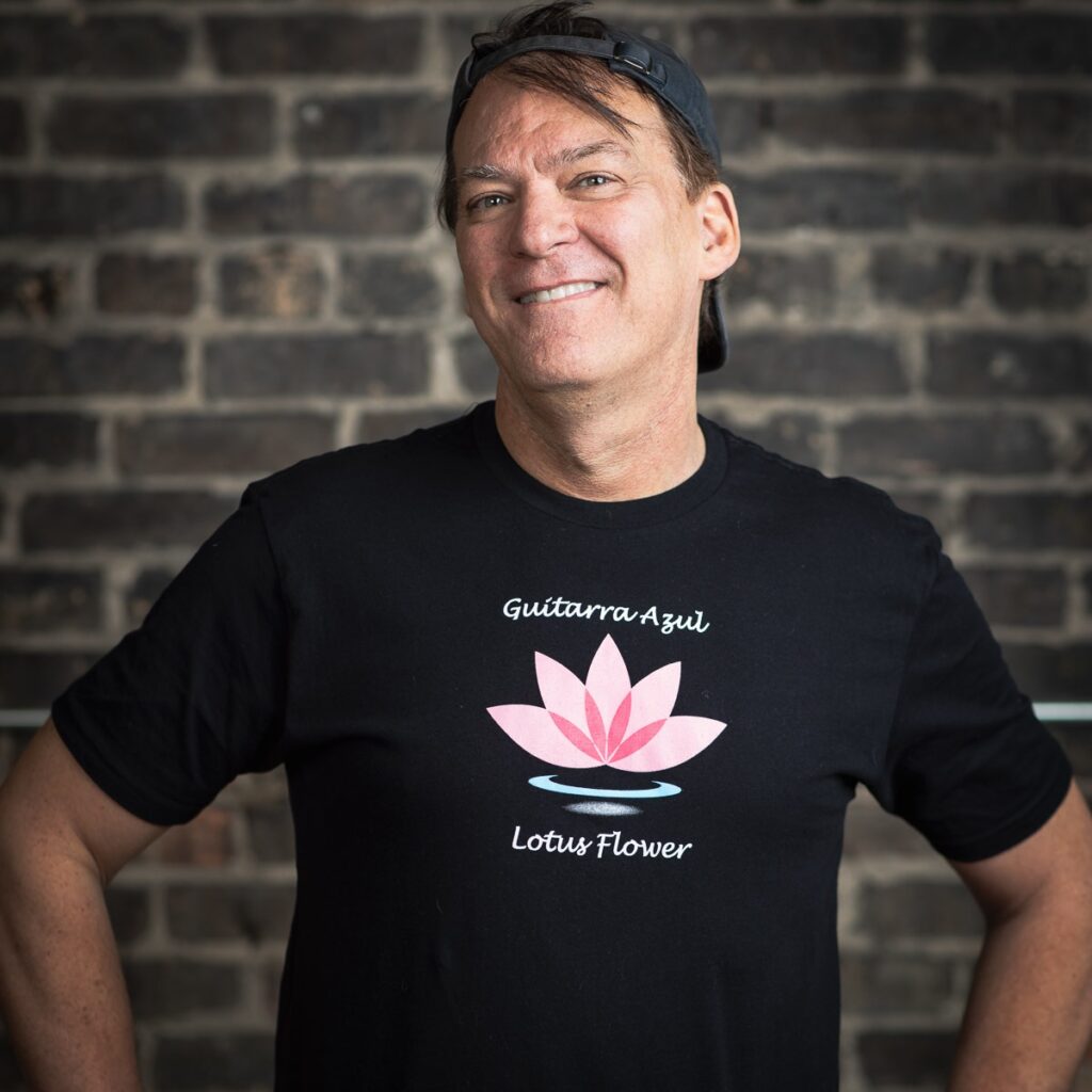 Man smiling in black t-shirt, brick background.
