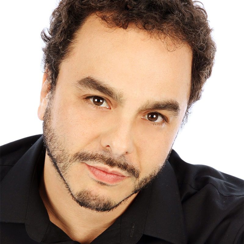 Man with curly hair and beard, smiling.